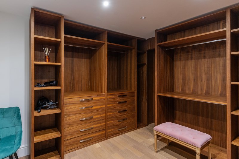 Large walk-in closet with wooden cabinetry, built-in storage, and upholstered bench seating