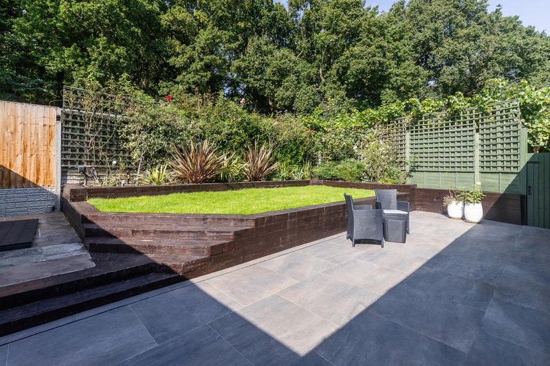 Modern garden patio with raised planter beds, stone paving and mature trees