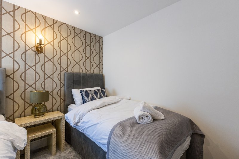 Modern bedroom with dark bed, geometric patterned accent wall, bedside table and wall sconce lighting