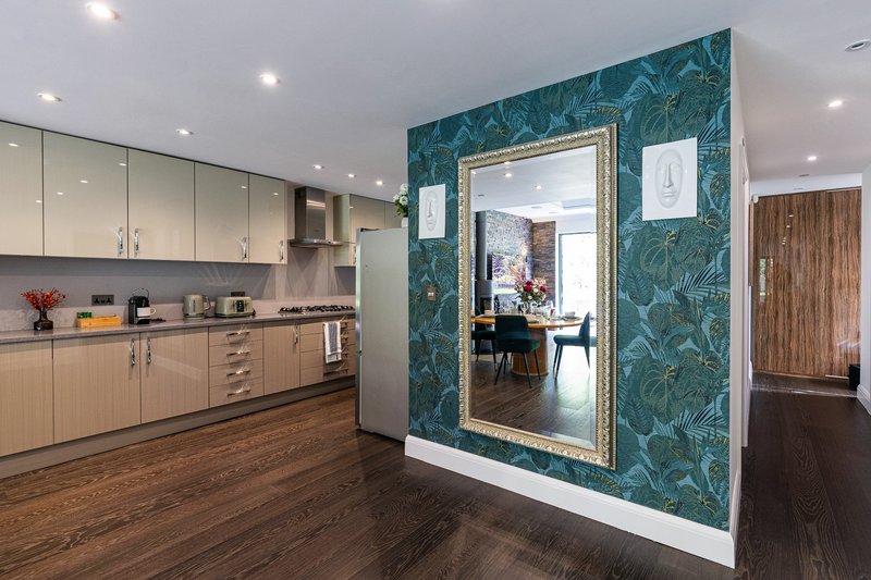 Modern kitchen with wooden cabinetry, stainless steel appliances, and teal patterned accent wall with mirror doorway