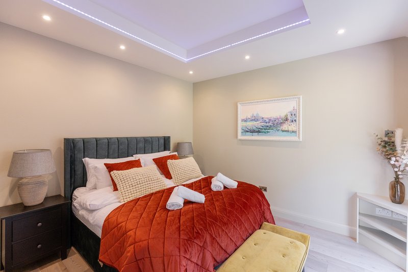 Modern bedroom with double bed, red quilt, grey headboard and ambient ceiling lighting