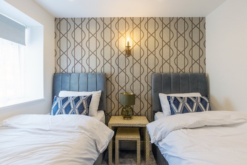 Twin bedroom with blue headboards, patterned accent wall, bedside table and wall sconce