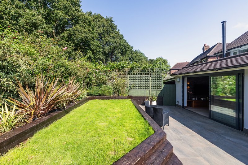 Modern garden with manicured lawn, raised beds, tropical plants, and contemporary house extension with dark cladding
