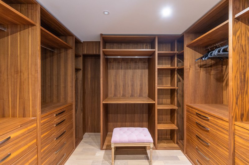 Spacious walk-in wardrobe with wooden cabinetry, shelving, and upholstered bench seat