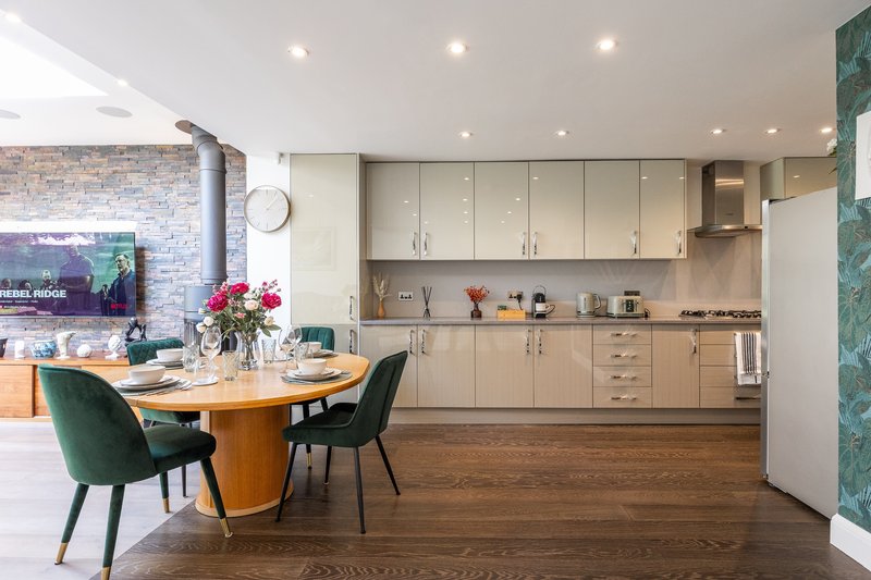 Modern open-plan kitchen and dining area with cream cabinetry, wooden dining table, and dark chairs