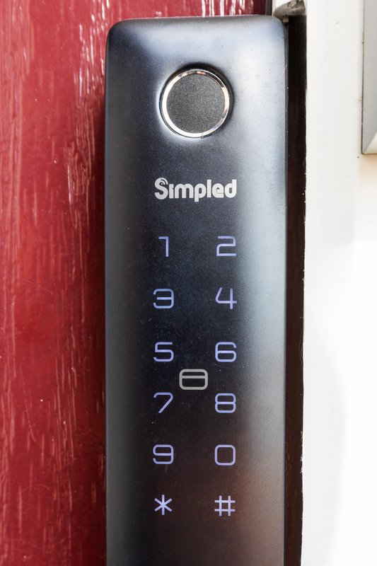 Black digital keypad lock mounted on red wooden door frame