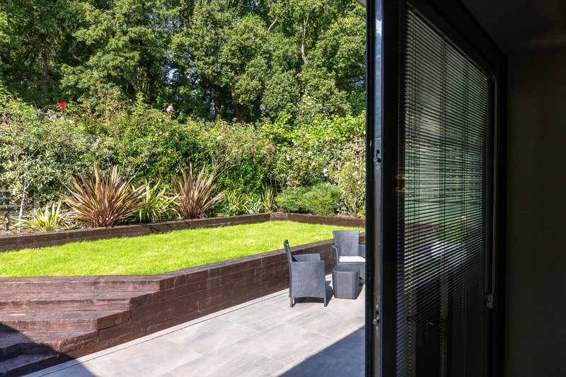 Patio area with garden furniture overlooking manicured lawn and mature trees