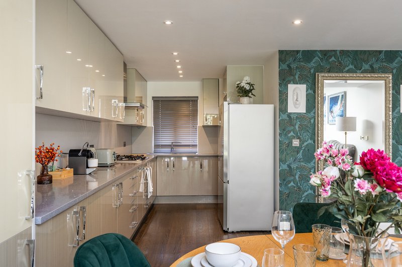 Modern kitchen with wooden dining table, white appliances, teal feature wall and fresh flowers