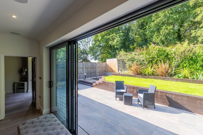 Modern patio area with large sliding glass doors, outdoor seating, and manicured garden beyond