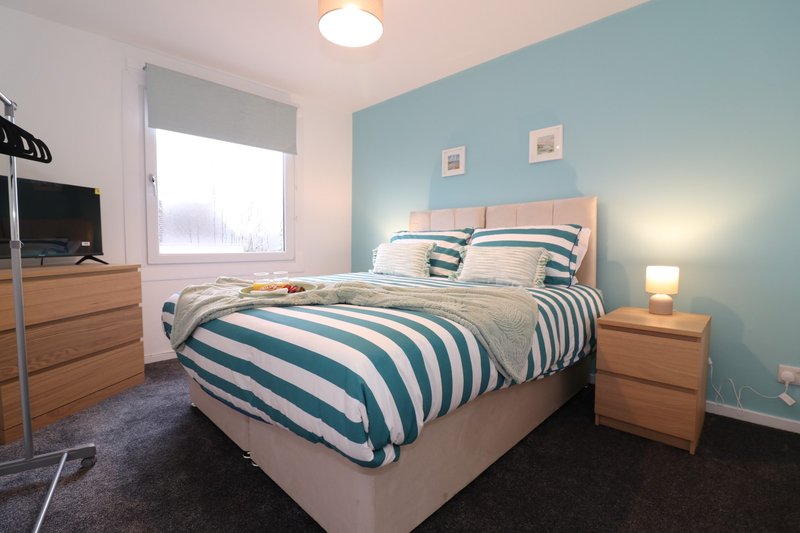 Modern bedroom with striped duvet, wooden furniture, blue accent wall and window