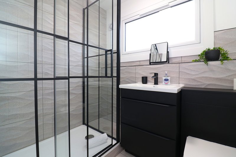 Modern bathroom with walk-in shower, black vanity unit, and frosted window