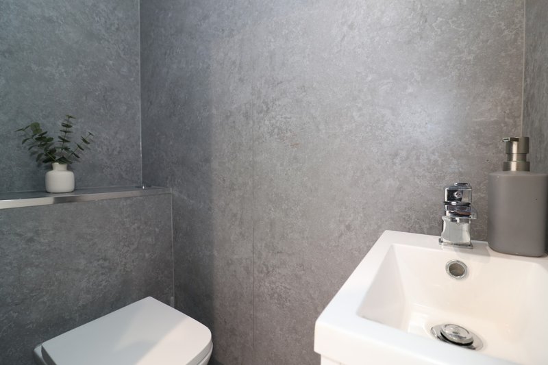 Modern bathroom with grey tile walls, white sink, toilet and chrome tap