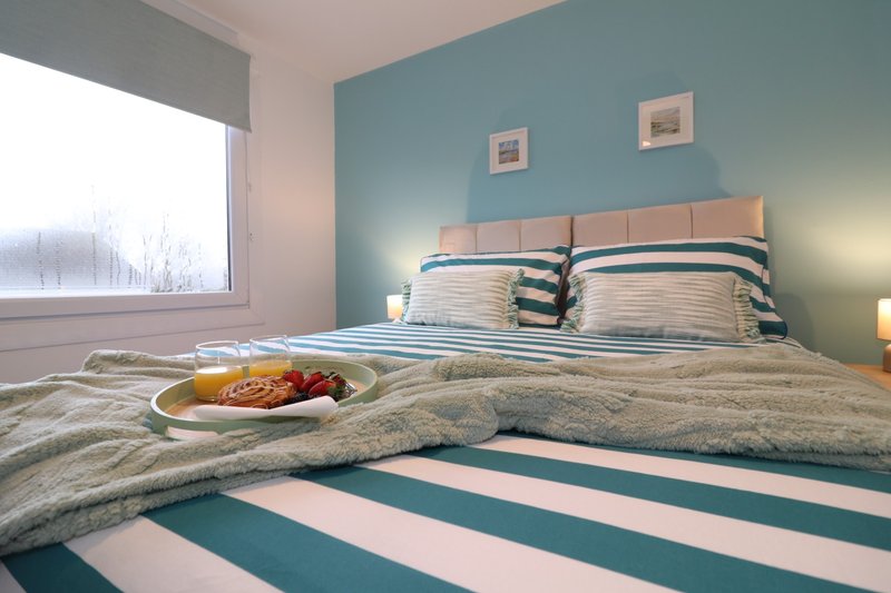 Modern bedroom with double bed, striped bedding, teal accent wall and bedside lamps
