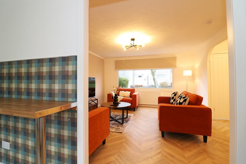 Spacious living room with orange armchairs, wooden floor, and large window with natural light