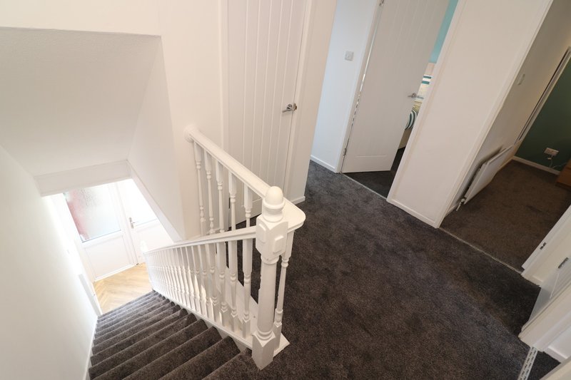 Staircase landing with white bannister, dark carpet, and multiple white doors
