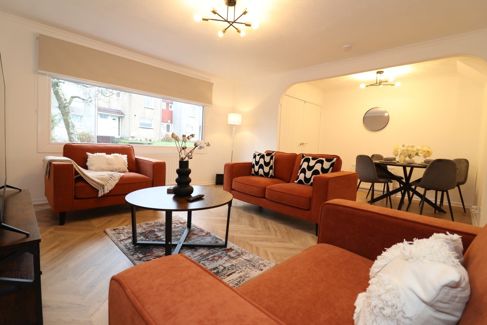 Open-plan living area with rust-colored sofas, round coffee table, wooden flooring and modern ceiling lights