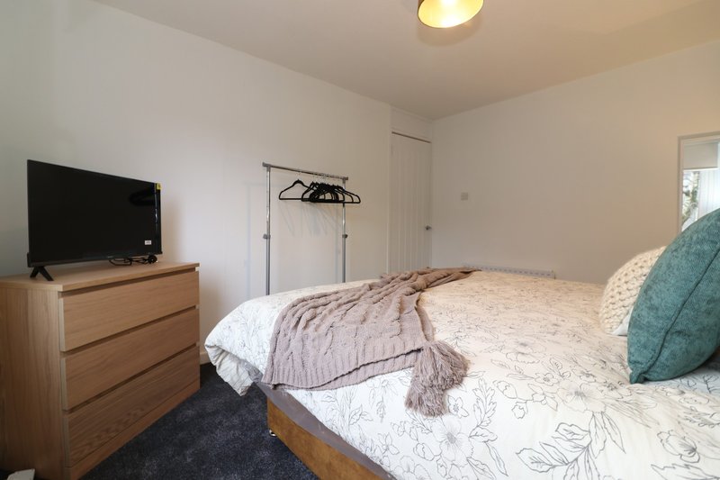 Bedroom with double bed, wooden dresser, TV, clothing rack and teal cushion
