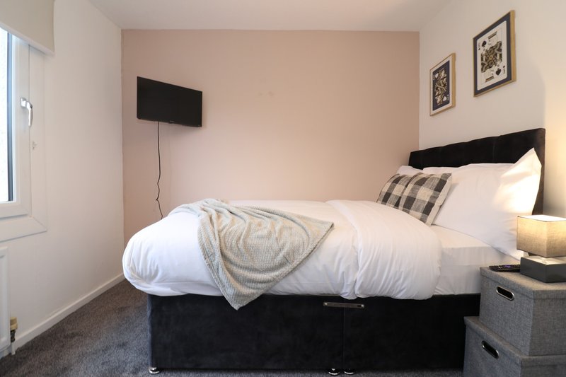 Bedroom with black bed frame, white bedding, wall-mounted TV, and framed wall art
