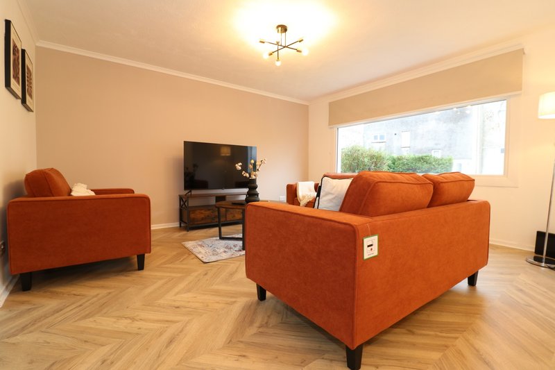 Bright living room with two orange sofas, TV stand, wooden floor and large window