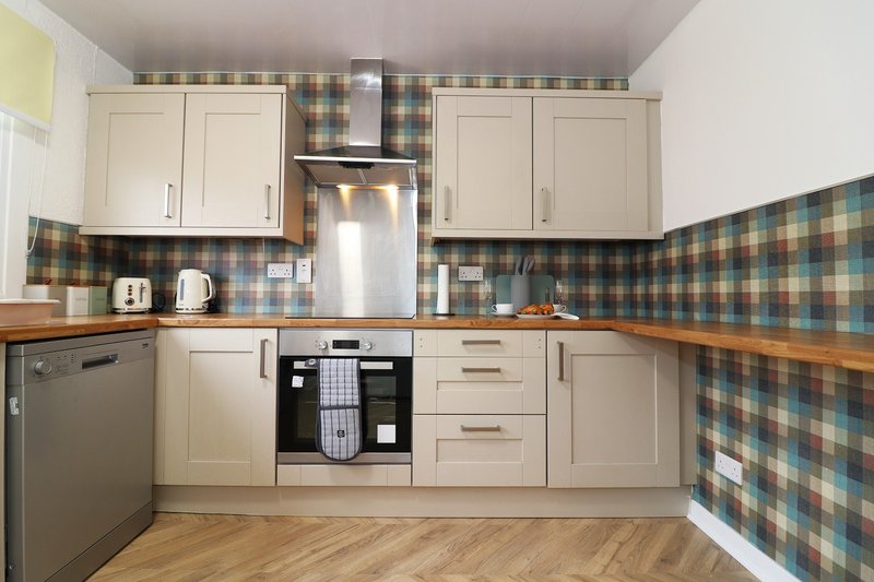 Modern kitchen with cream cabinets, stainless steel appliances, checkered tile backsplash and wooden counters