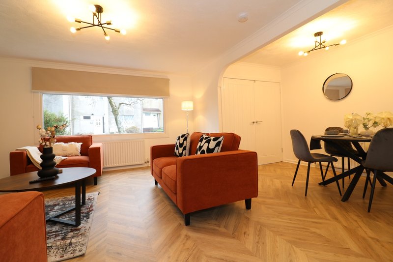 Open-plan living room with rust-colored sofa, dining area, wooden flooring and natural light