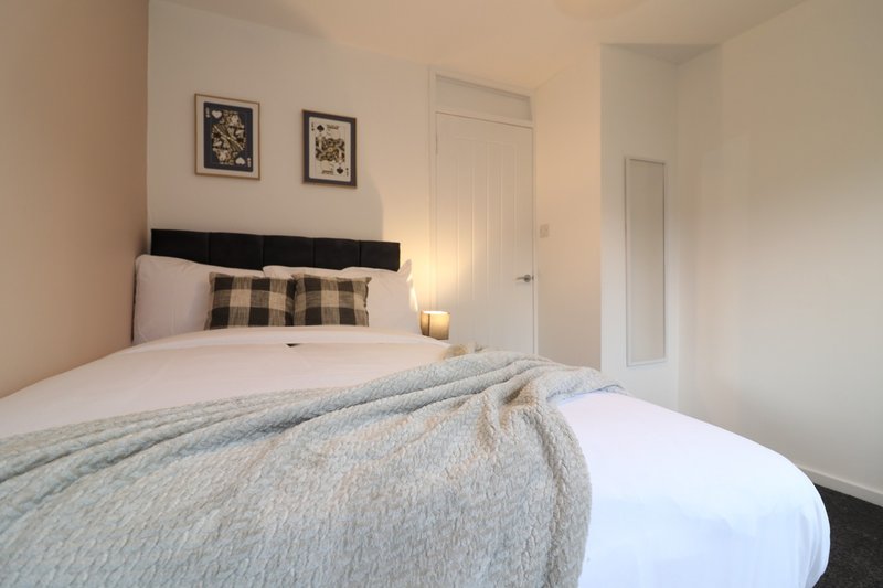 Bedroom with double bed, black headboard, patterned cushion, bedside lamp and framed wall art