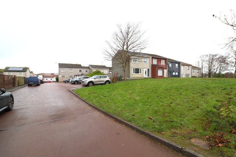 Modern residential building exterior with driveway, parked cars, and surrounding green lawn