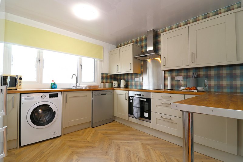 Modern kitchen with cream cabinets, wooden worktops, integrated appliances and checked backsplash