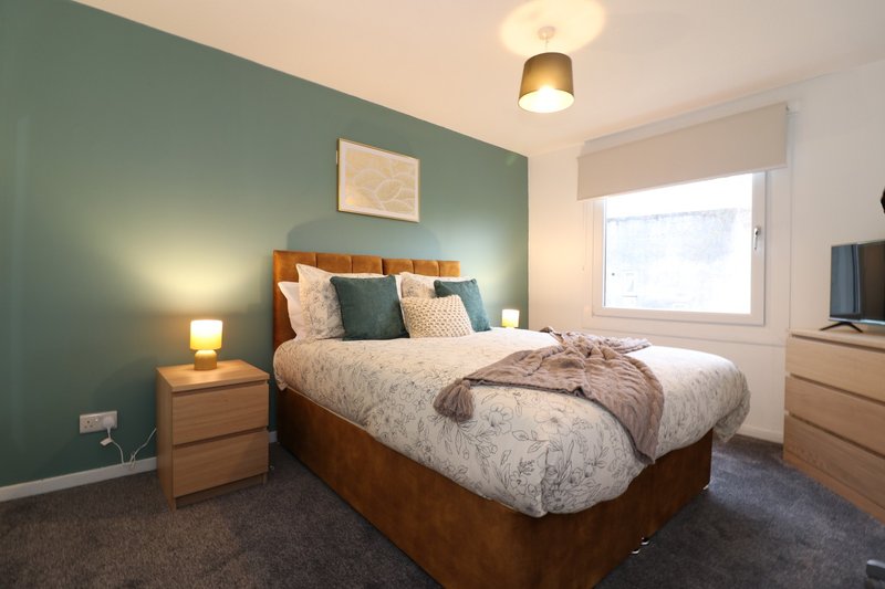 Bedroom with wooden bed, green accent wall, bedside lamp, and window with white blinds