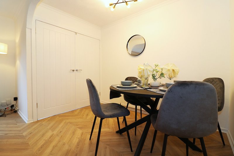 Dining room with black table, upholstered chairs, wooden floor and wall clock