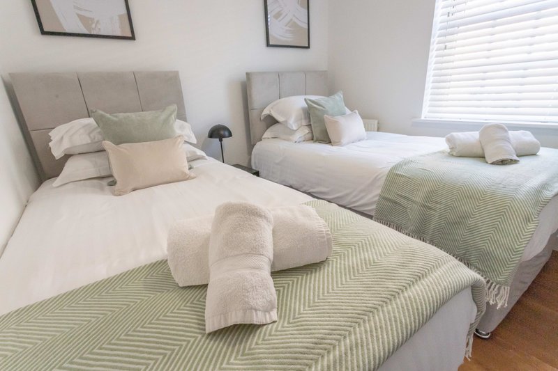Twin bedroom with two single beds, neutral bedding, pillows and rolled towels