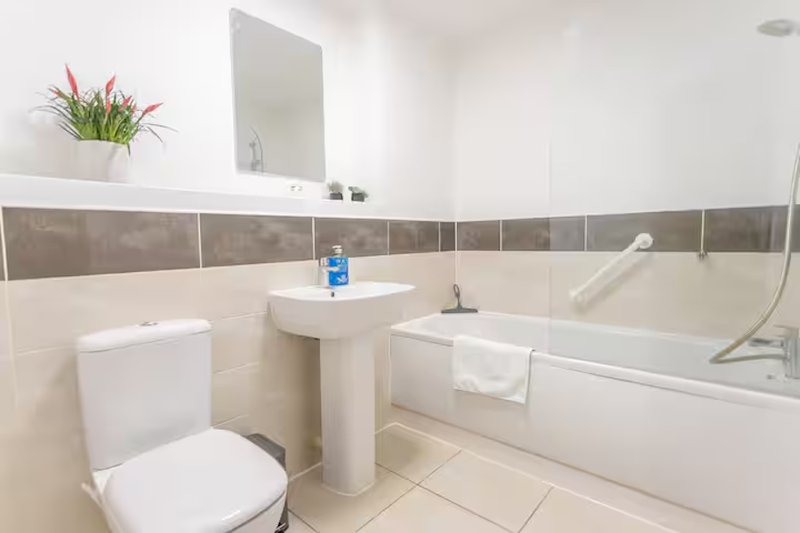 Modern bathroom with white toilet, pedestal sink, bathtub, mirror and potted plant