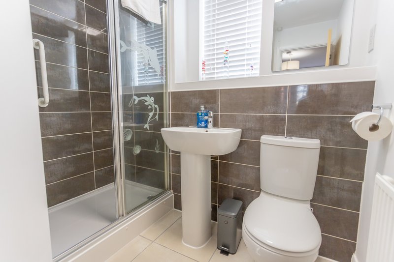 Modern bathroom with shower enclosure, pedestal sink, toilet and brown tile walls