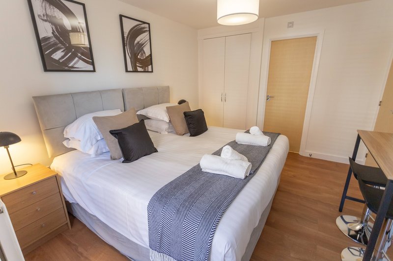 Spacious bedroom with double bed, white bedding, black cushions, wooden nightstands and hardwood flooring
