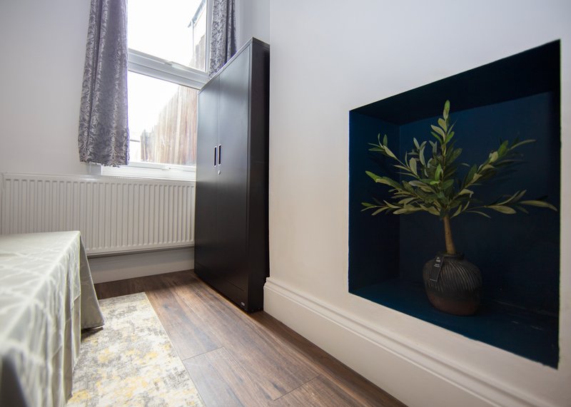 Bedroom with single bed, black wardrobe, window with radiator and wall art