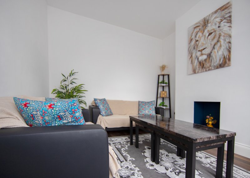 Bright living room with black sofa, colorful cushions, coffee table, and lion wall art