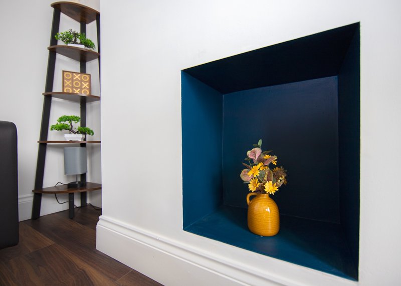 Modern living room with dark wood shelving unit, potted plants, and navy blue wall niche with yellow flowers