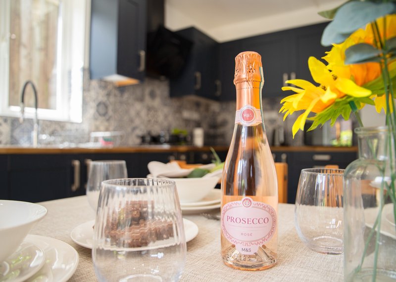 Modern kitchen with bottle of prosecco, glasses, flowers and place settings on counter