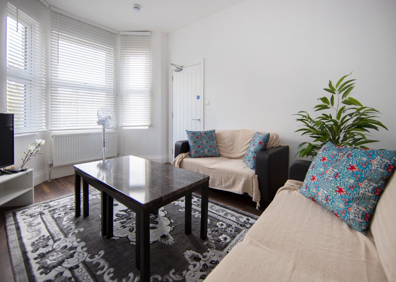Bright living room with black coffee table, beige sofas, blue patterned cushions, potted plant, and large windows