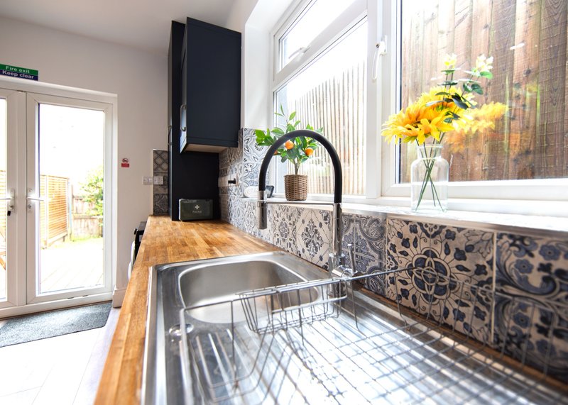 Modern kitchen with stainless steel sink, wooden countertop, patterned backtile and yellow flowers in vase