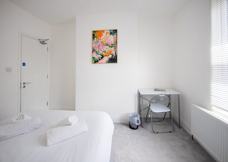 Bright bedroom with white bed, folded towels, framed flower artwork, and window with blinds