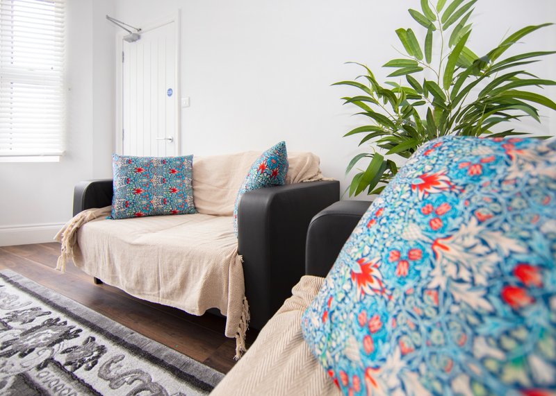 Living room with black sofa, patterned cushions, cream throw blanket, potted plant and window