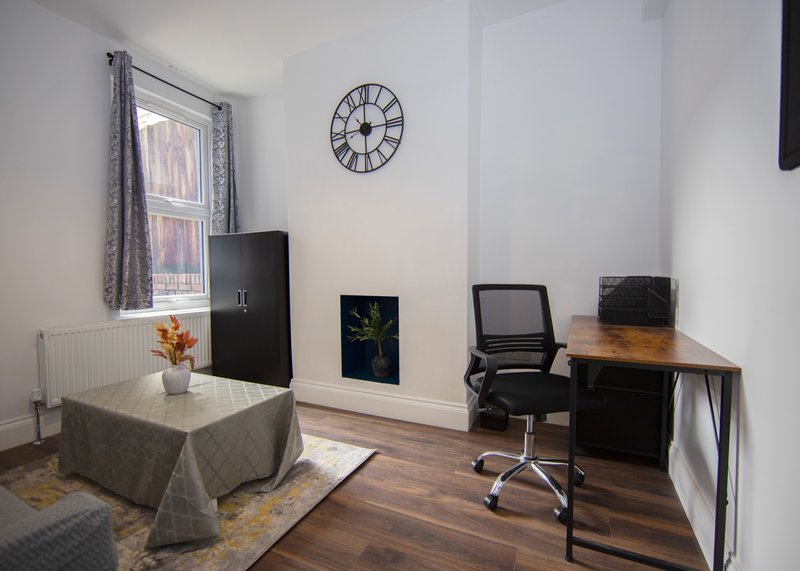 Bright home office with desk, office chair, wall clock, window with curtains and wooden flooring