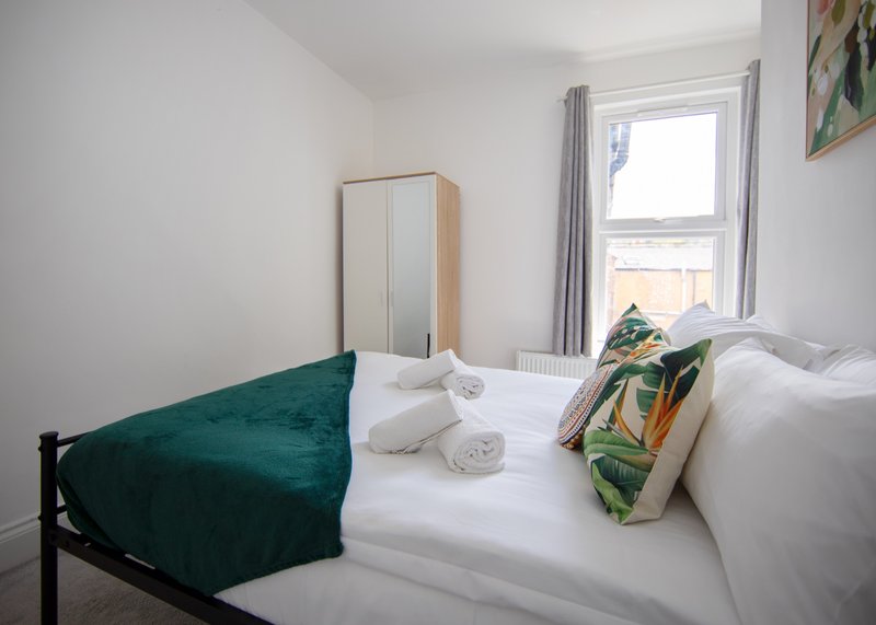Bright bedroom with double bed, white linens, teal cushion, wardrobe and window