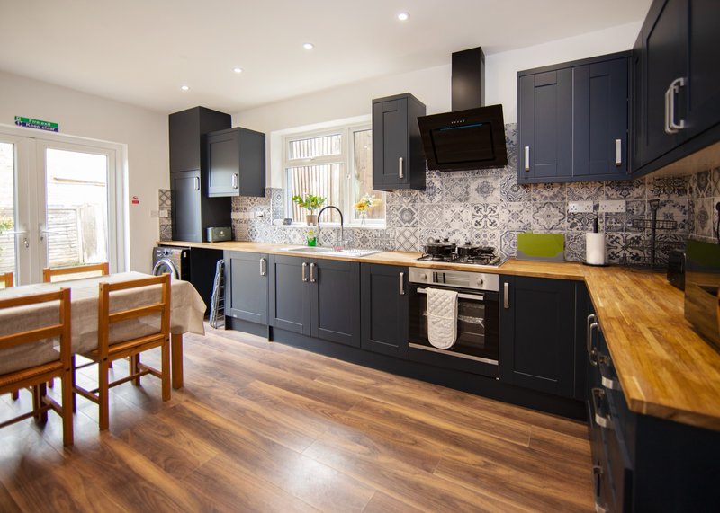 Modern kitchen with black cabinetry, wooden countertop, patterned backtile and dining area