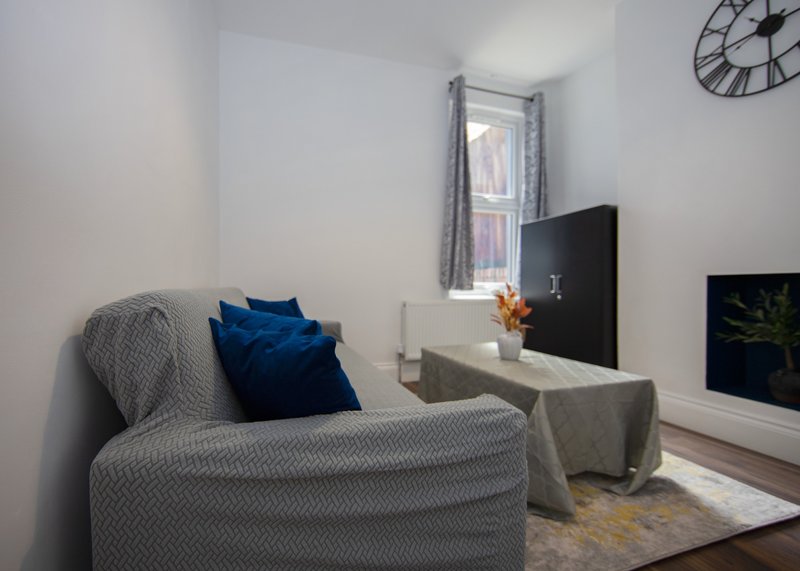 Modern living room with gray upholstered armchair, blue cushions, wall-mounted TV, and window with curtains