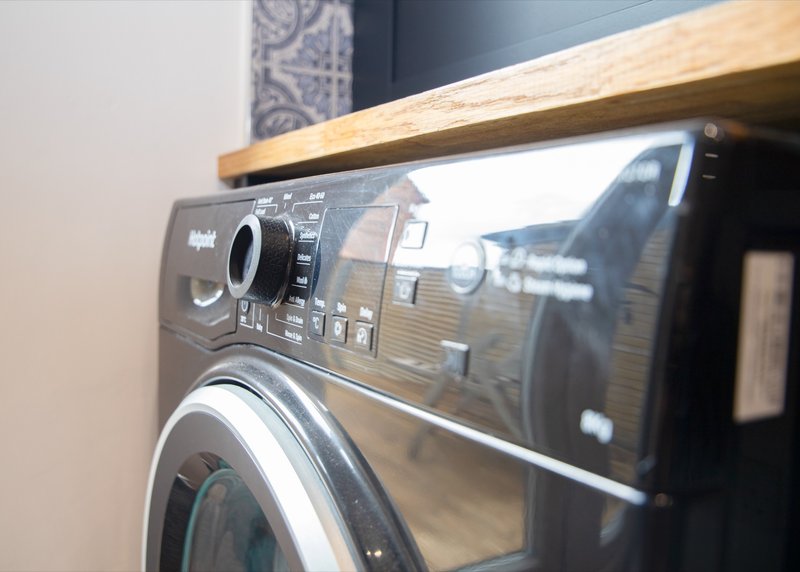 Modern black washing machine under wooden shelf in utility room