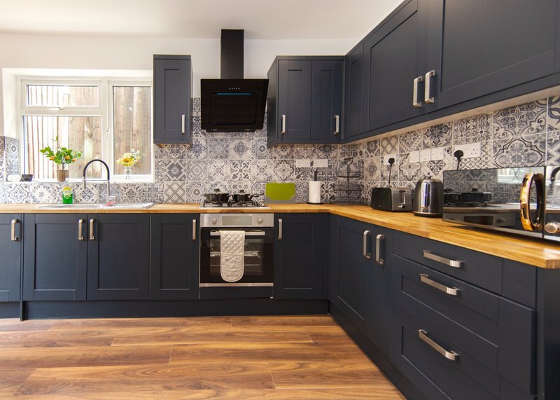 Modern kitchen with dark cabinetry, patterned backtile, wooden countertop and stainless steel appliances