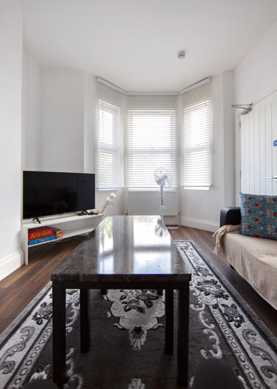 Bright living room with black dining table, TV on wooden stand, bay windows and cream sofa