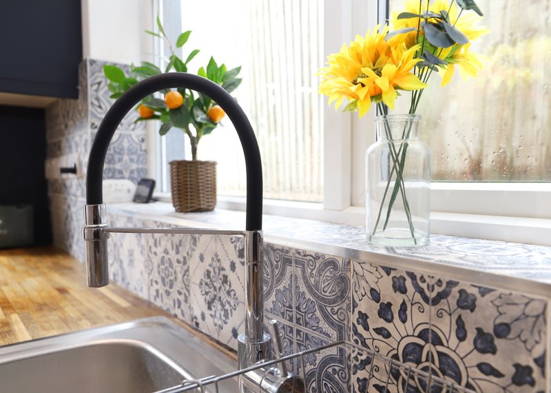 Modern kitchen sink with black faucet, decorative backsplash, and fresh flowers in vase by window